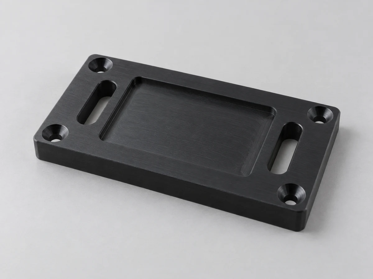 Illustration générée par l'IA d'une plaque de montage rectangulaire en acétal noir, de quatre trous fraisés dans les coins, de deux fentes oblongues et d'une face rectangulaire encastrée peu profonde